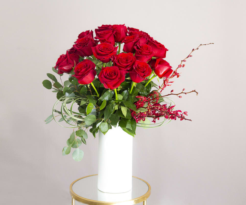 Two Dozen roses.. and red orchids in a tall- white ceramic vase.