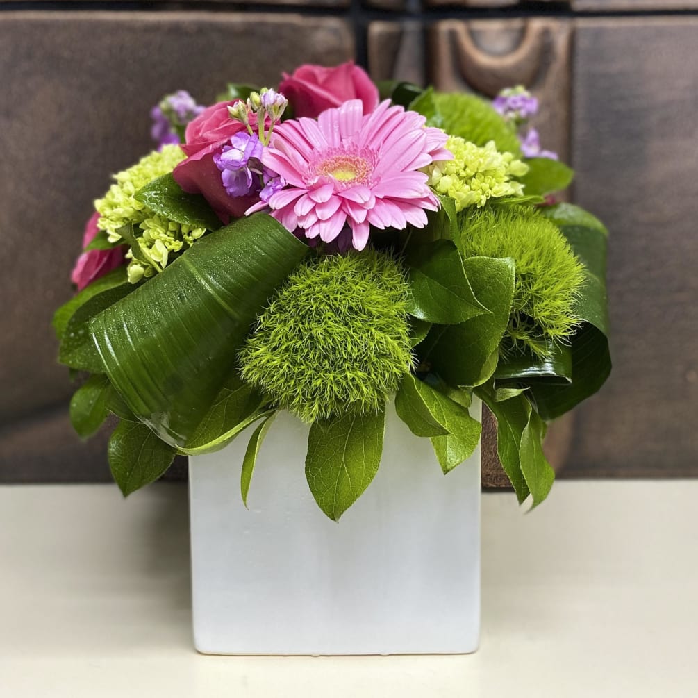 Hot pink roses, pink Gerber daisies, and hydrangeas in white ceramic cube.
