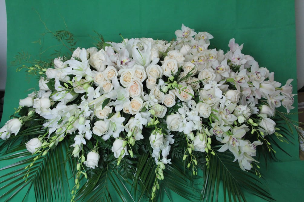 Casket flowers arranged with white roses, lilies and orchids falling on one