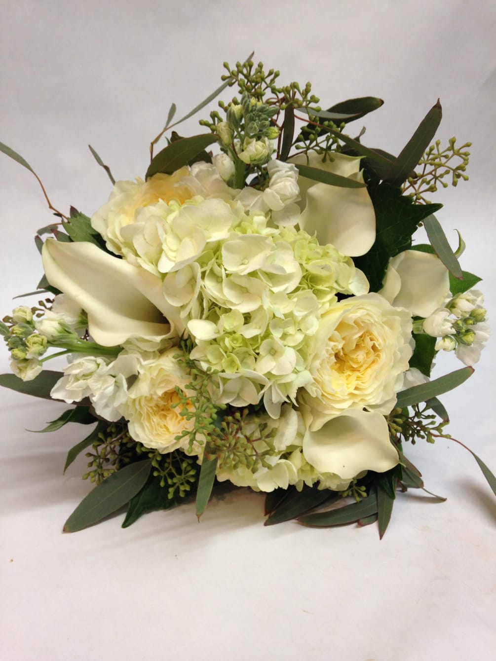 Calla lillies, garden roses, hydrangea, and stock are surrounded by seeded eucalytus