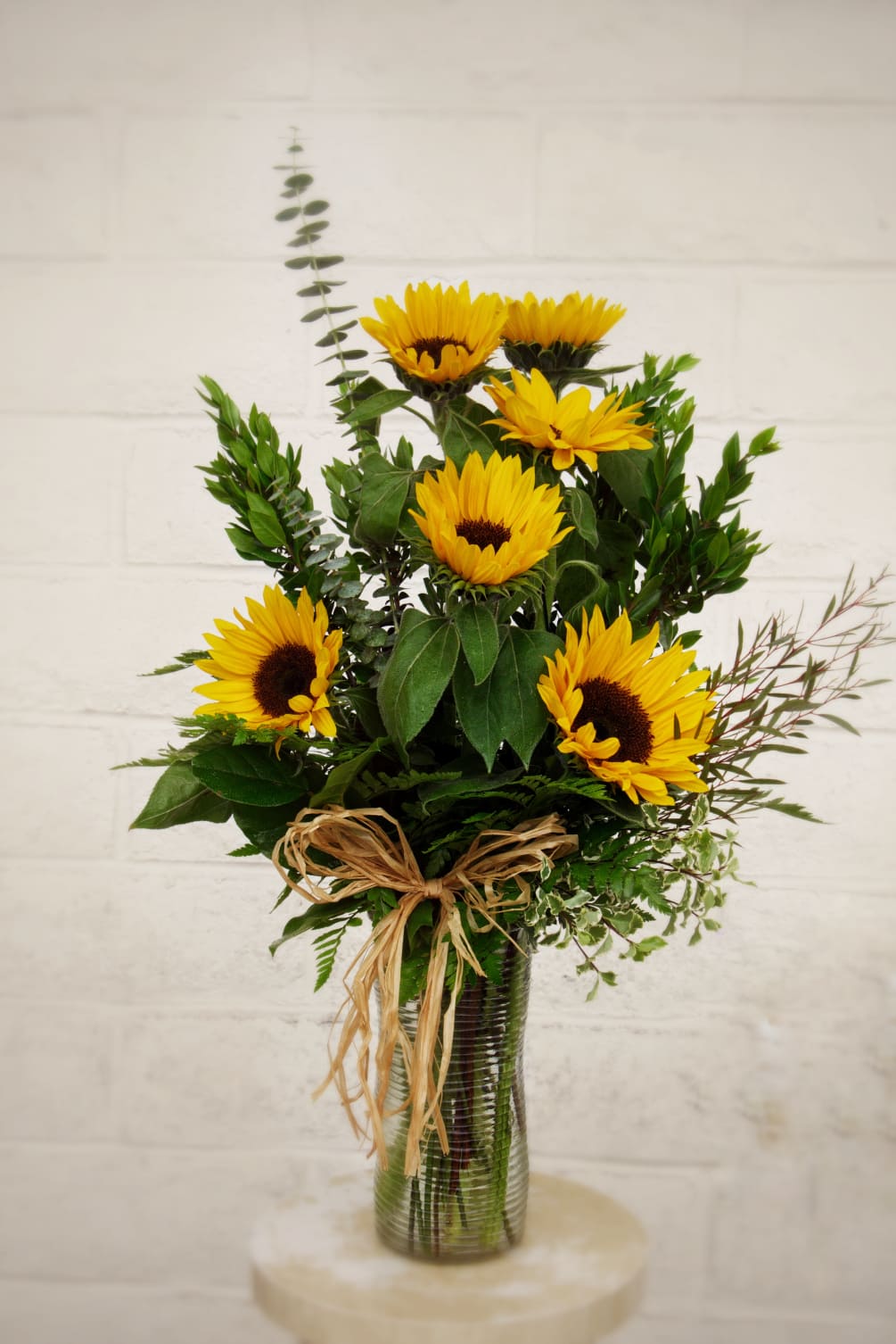 Sunflowers and variety of greens in a tall vase