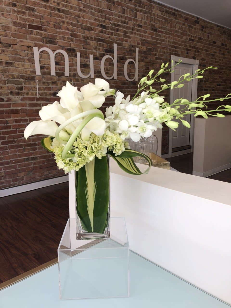 Designers choice arrangement of white and green flowers keeping in this signature