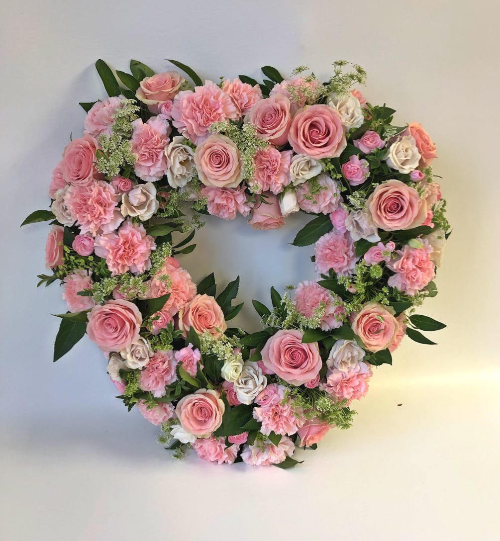 An 18&quot; heart wreath with pink roses, white filler and pink carnations.