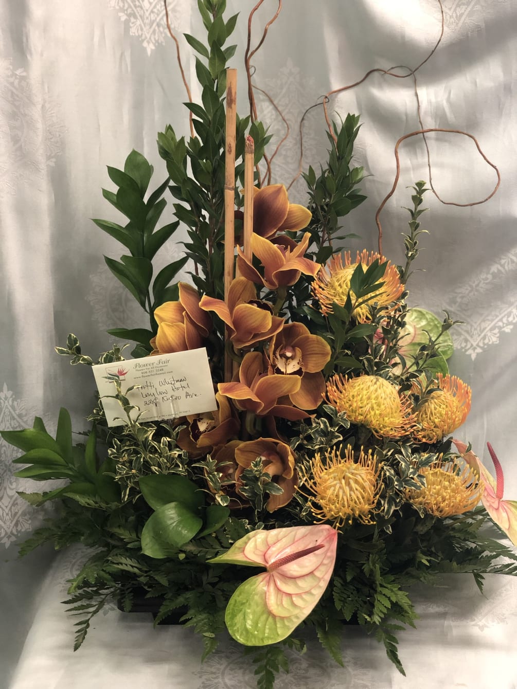 All tropical arrangement with yellow protea, orange cymbidium orchids accented with anthuriums.