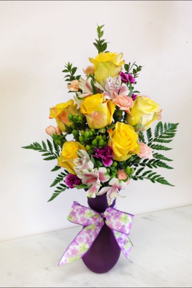 Yellow roses in purple vase with ribbon arranged with carnations and alstroemeria.

Flowers