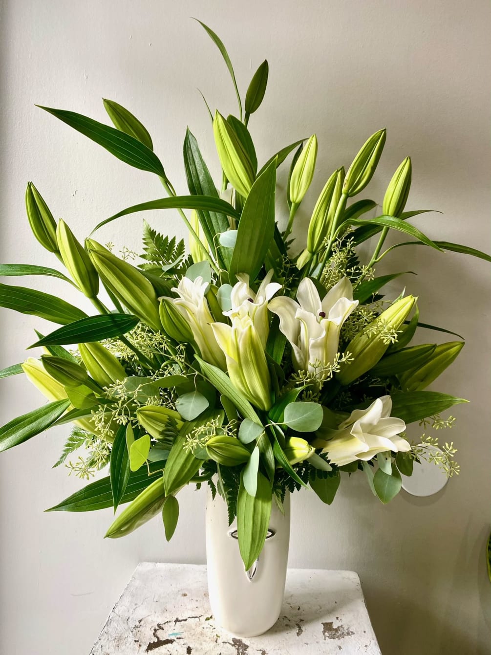 A tall arrangment of pure white lilies and delicate  seeded eucalyptus