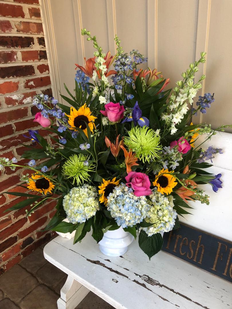 Tall and showy funeral display filled with bright summer colors. Light Blue