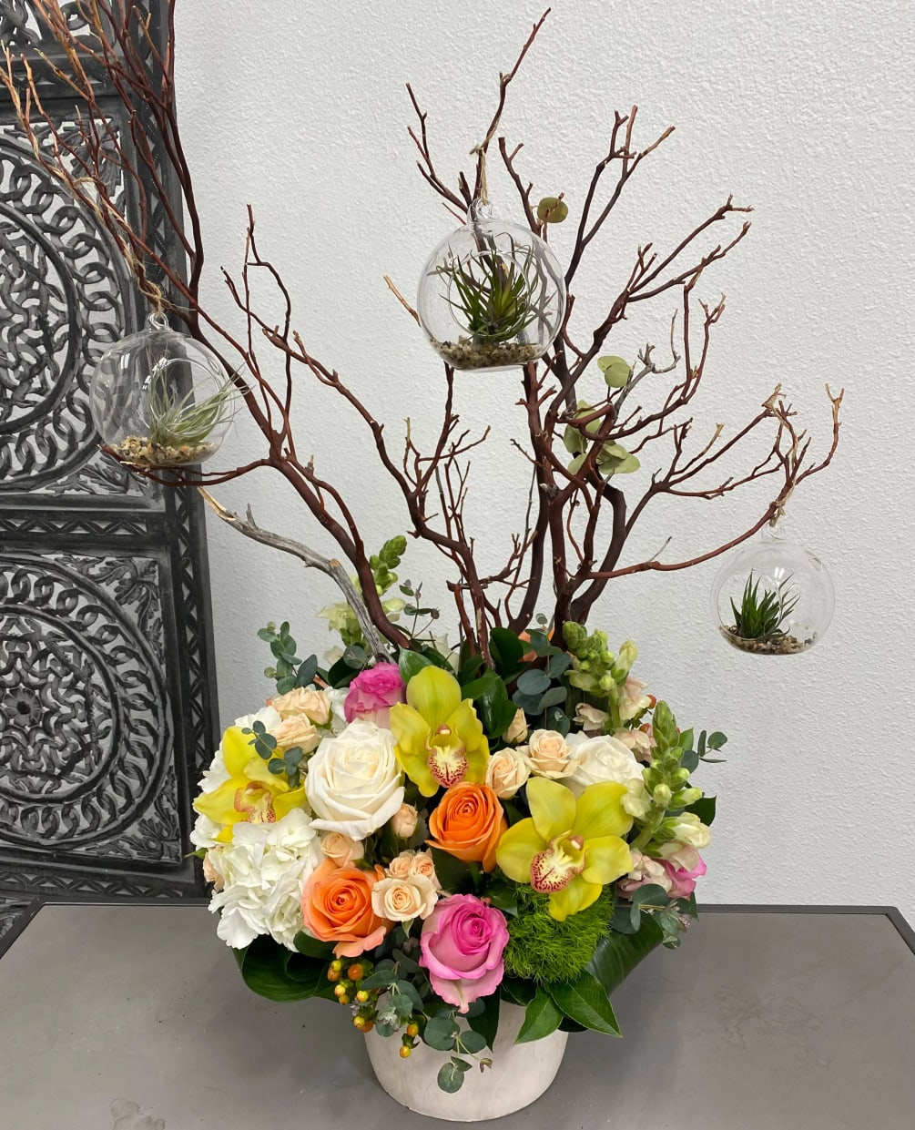 This arrangement includes a vibrant variety of flowers and a manzanita branch