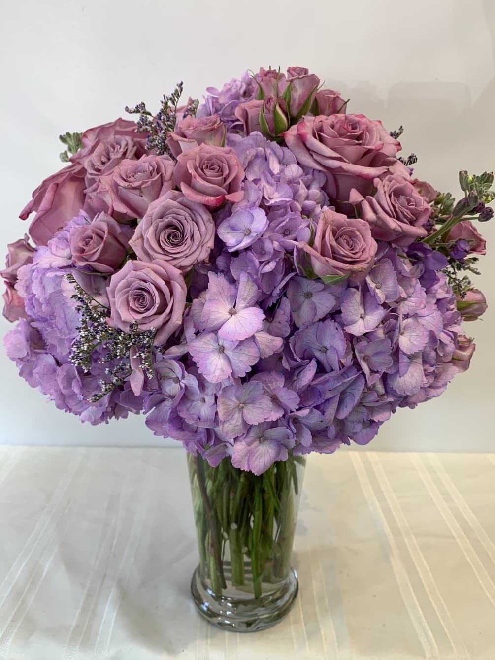Lavender Hydrangea, Roses, Spray Roses, Stocks, Caspia arranged nicely in clear glass