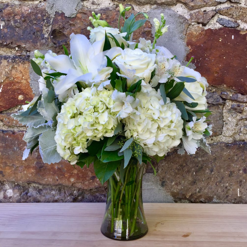 A stately white mix of white hydrangea, roses, lilies, and dusty miller