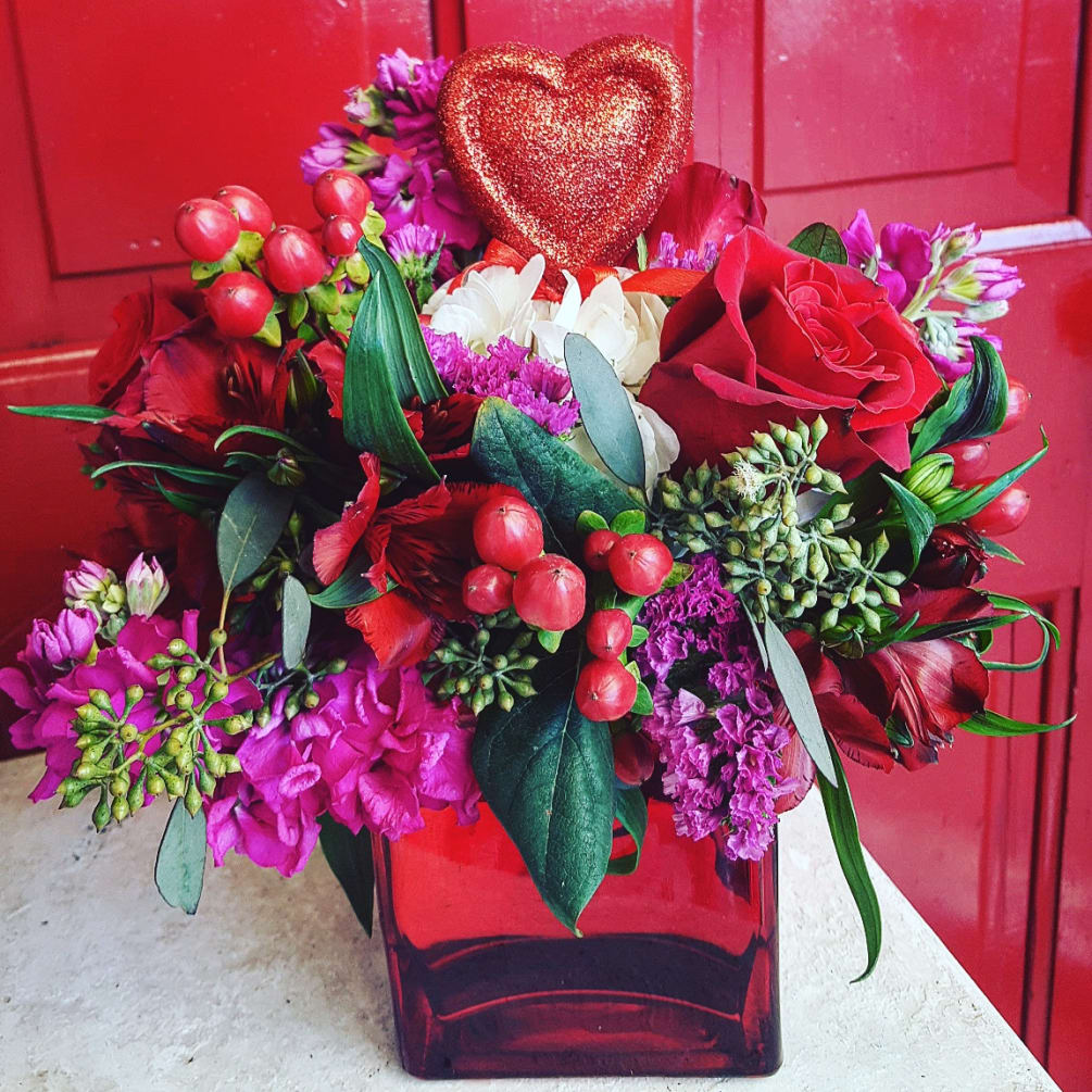 A variety of red roses, alstromeria, berries, and hot pink pops of