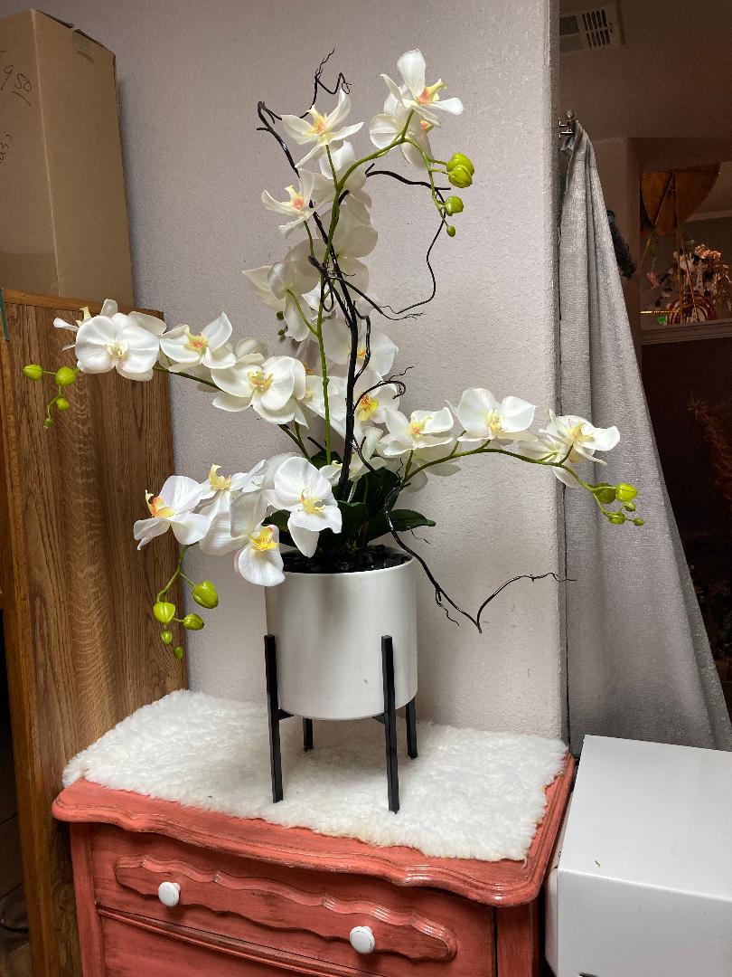 White silk orchids in white ceramic container on black stand.