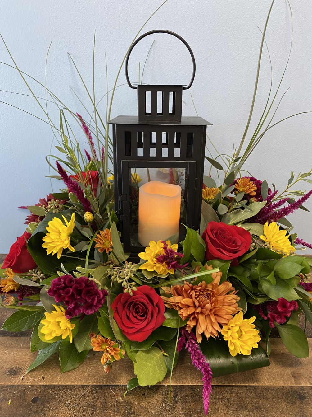 Beautiful arrangement of seasonal flowers around a lantern with battery operated candle.