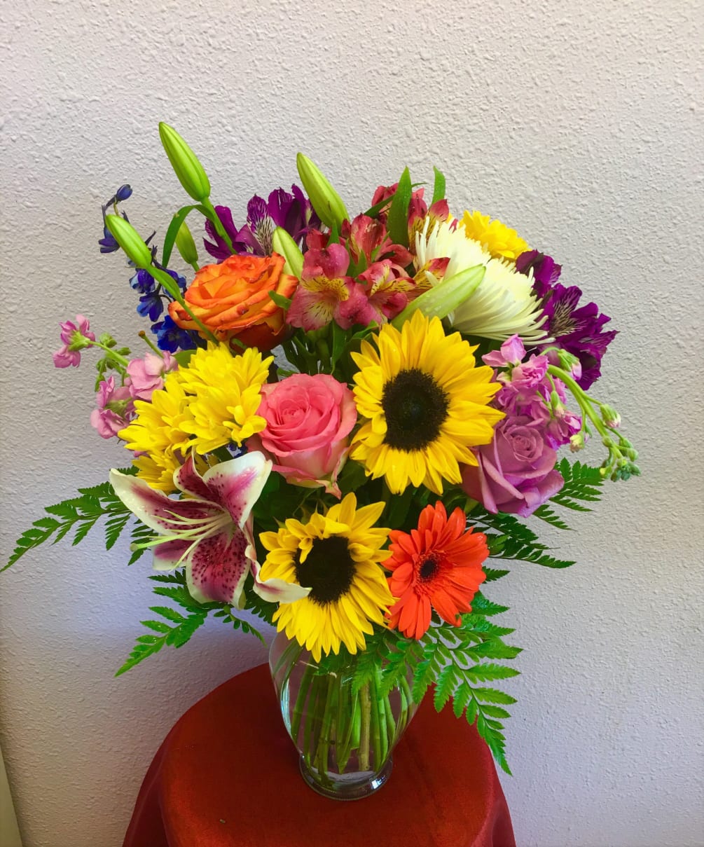 A colorful arrangement containing sunflowers, roses, lilies, gerbs, etc..