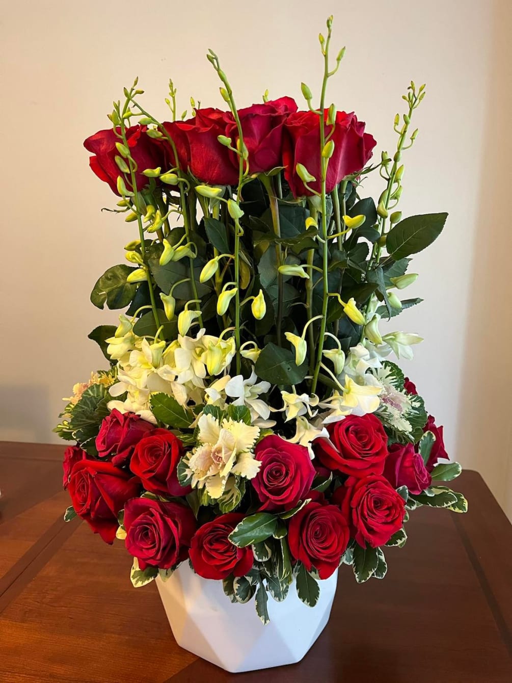 This arrangement includes red and hot pink roses, dendrobium orchids, Cabbages