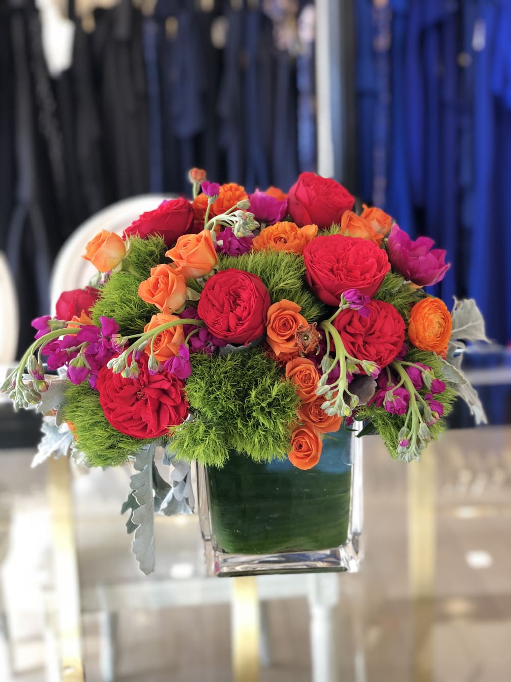 Sq glass vase featuring red Garden roses, orange roses, green dianthus, anemones