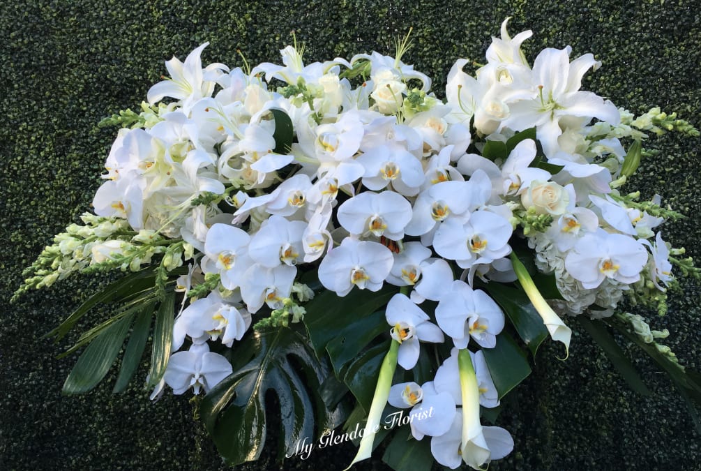 This casket arrangement includes white orchids, stargazer lilies, calla lilies, and hydrangeas.