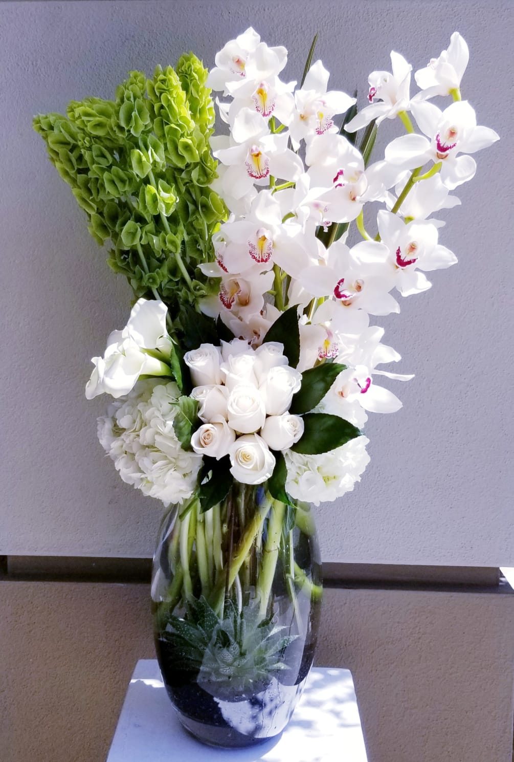Tall arrangement composed of white cymbidium orchids, bells of Ireland, roses, hydrangeas
