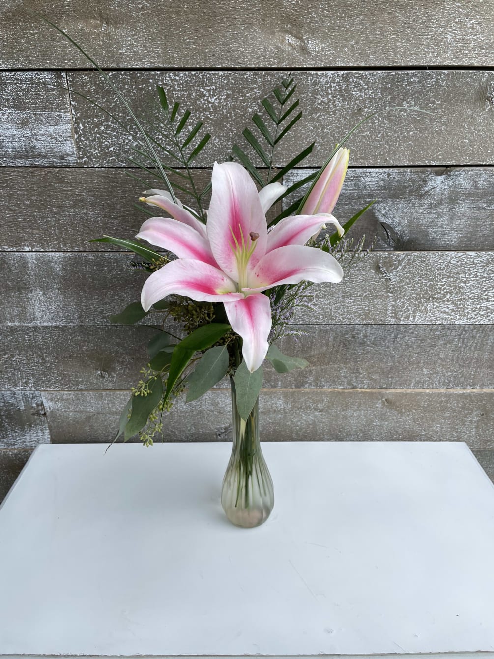 A simple pink stargazer in a bud vase with greens and filler