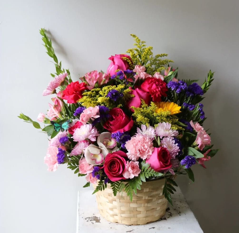A bright, beautiul basket arrangment with hot pink roses, sunflowers, carnations, cymbidium