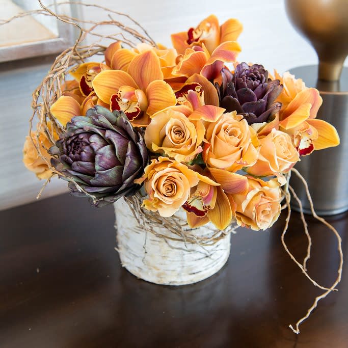 Mustard roses, cymbidium orchids, artichoke hearts, and curly willow accents in a