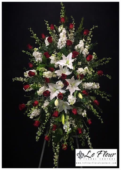 A tall sympathy standing spray filled with red roses and mixed white