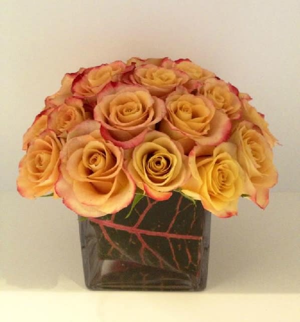 An arrangement of all sunset tone roses in a leaf lined vase.