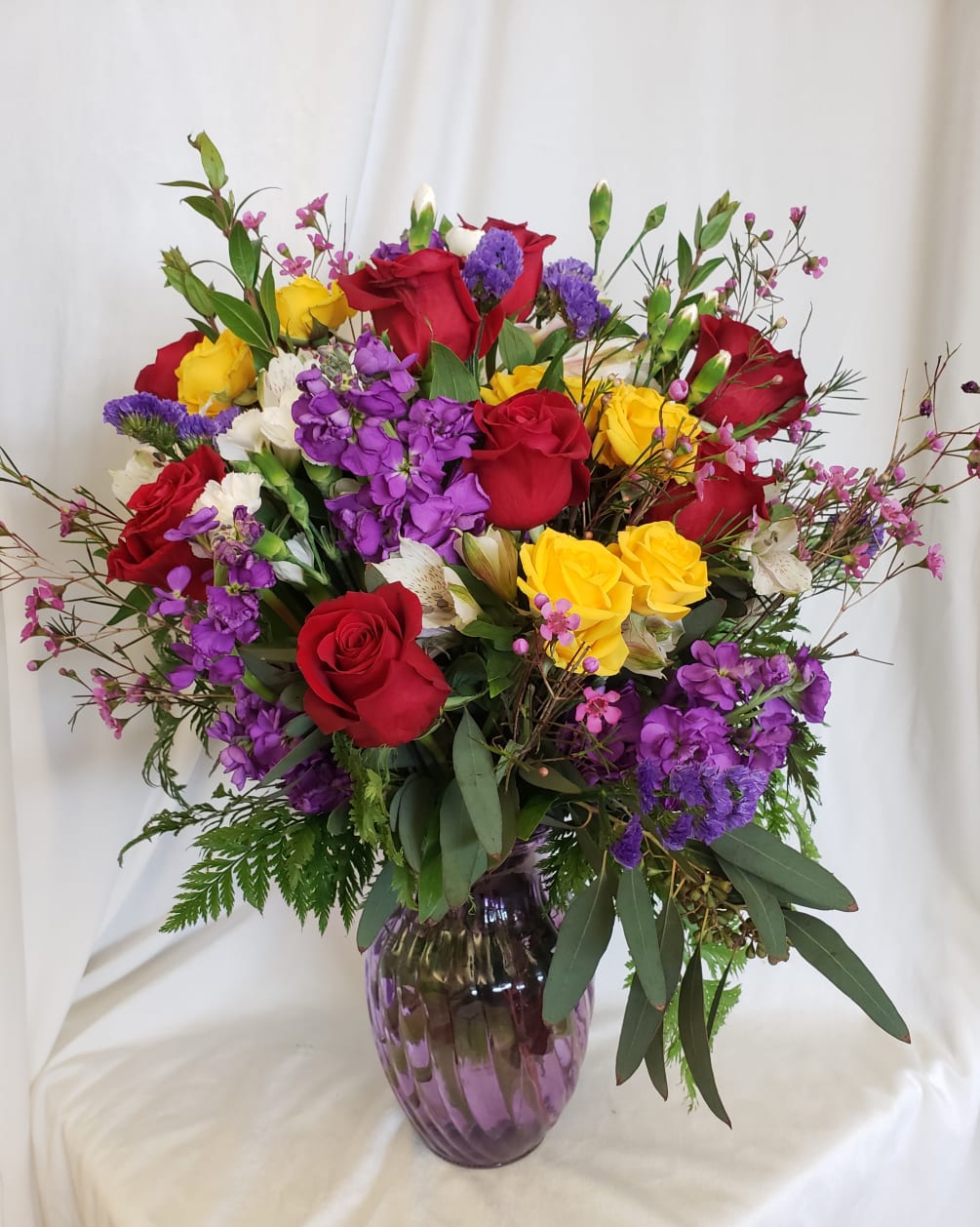 Bright and cheery arrangement of yellow spray roses, red roses, purple stock