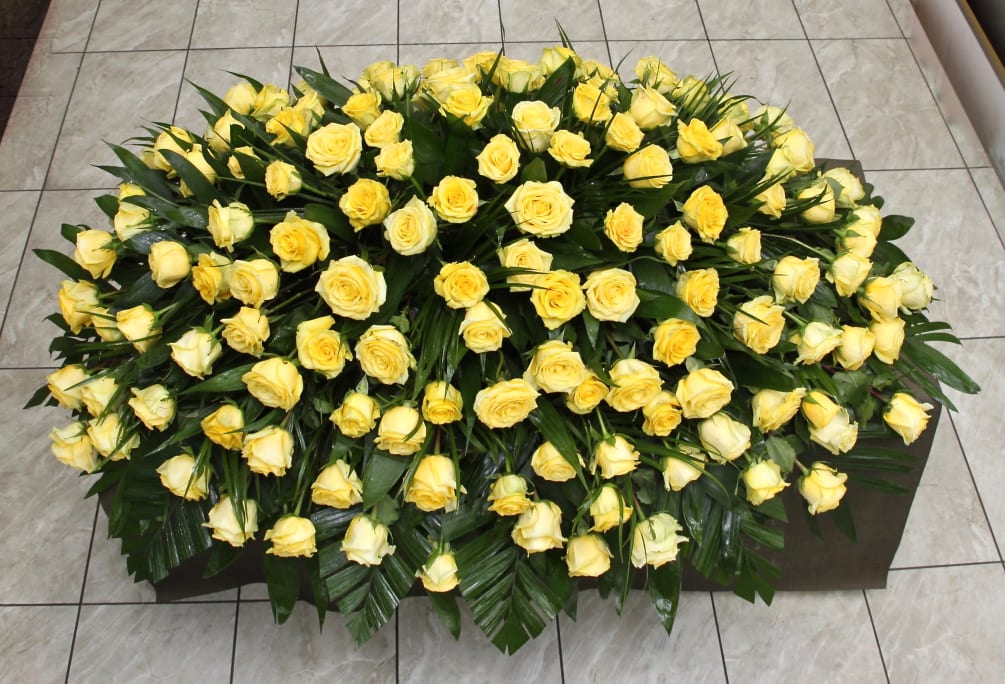 This casket arrangement contains bright yellow roses and seasonal greens. 