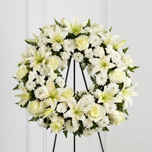 This wreath features Bright white roses, lilies, mini carnations and pom cushions