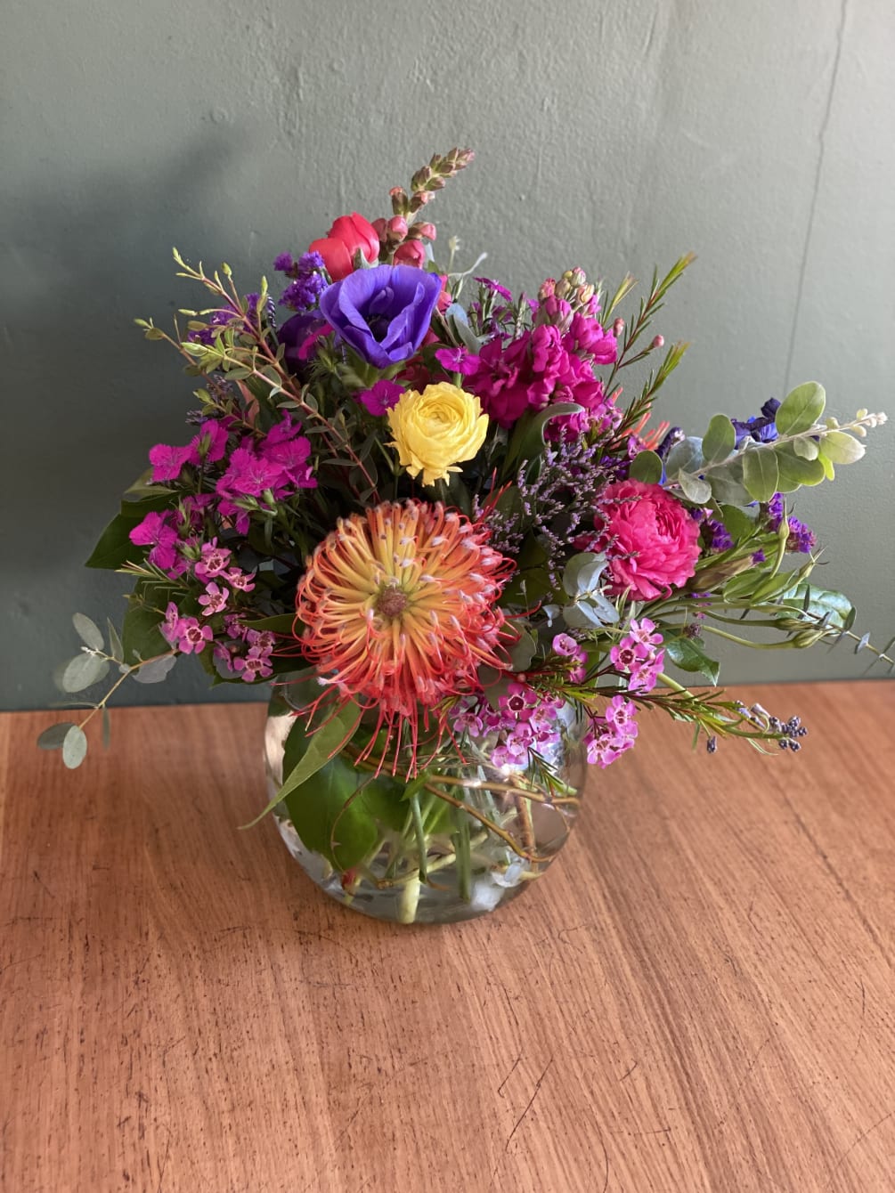 An arrangement of wild flowers that include pincushion, snap dragon, roses, ranunculus