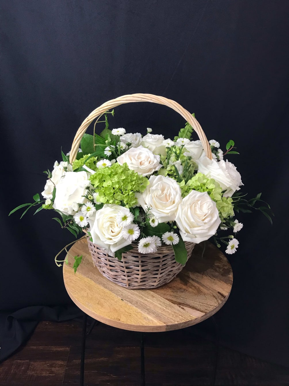 A lovely basket full of white roses and green hydrangeas nested in