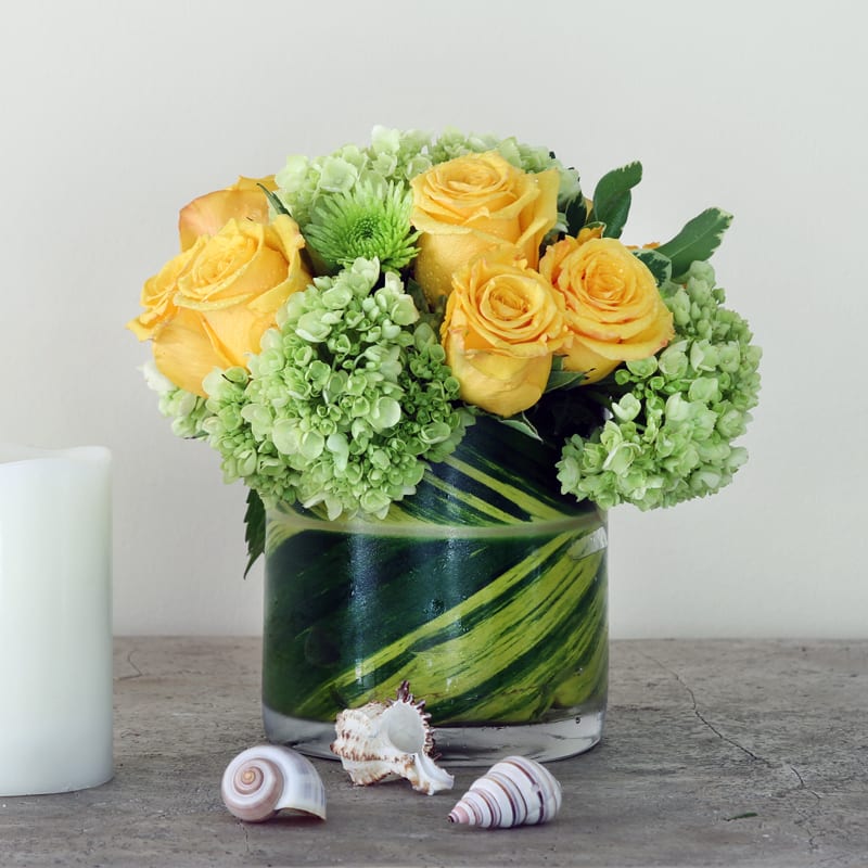 Round design with bright yellow roses and lush green hydrangeas in a