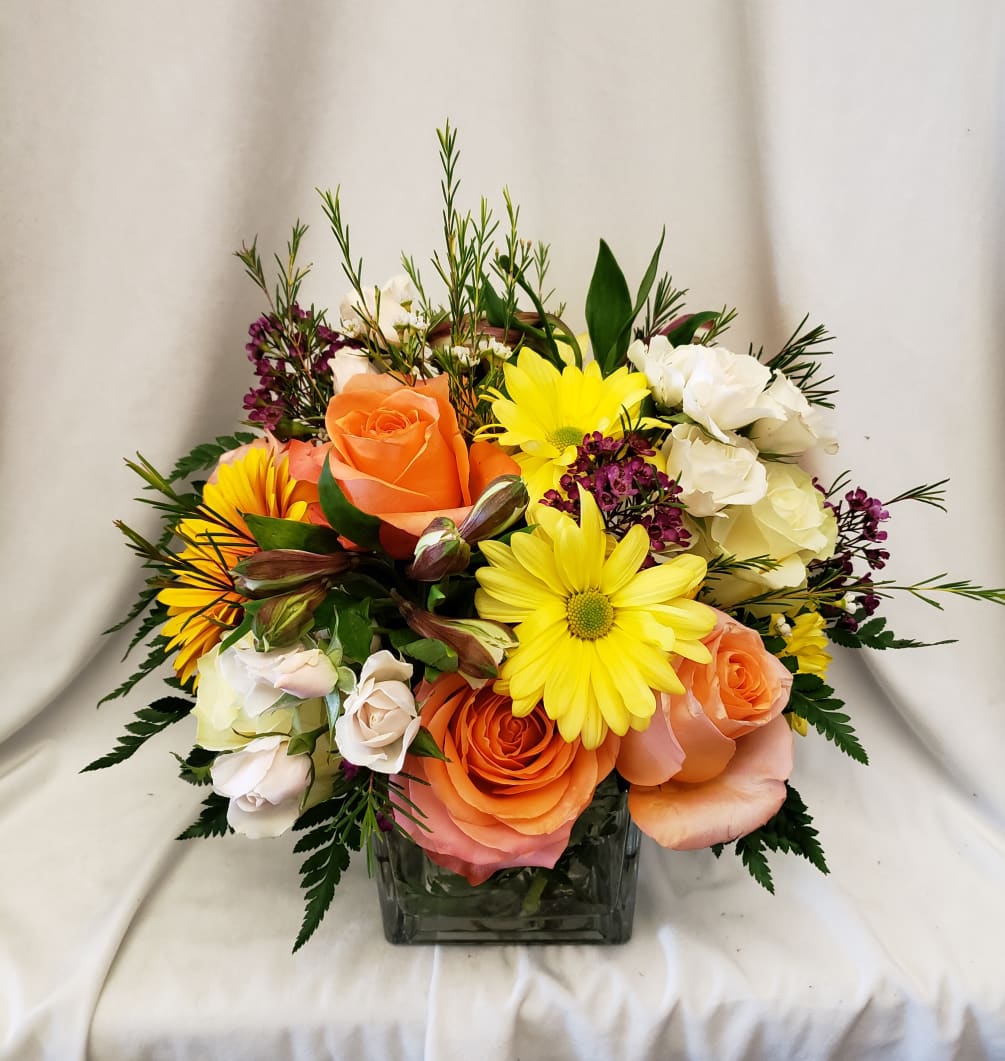 Bright and sunny floral arrangement in a glass cube with roses, daisies