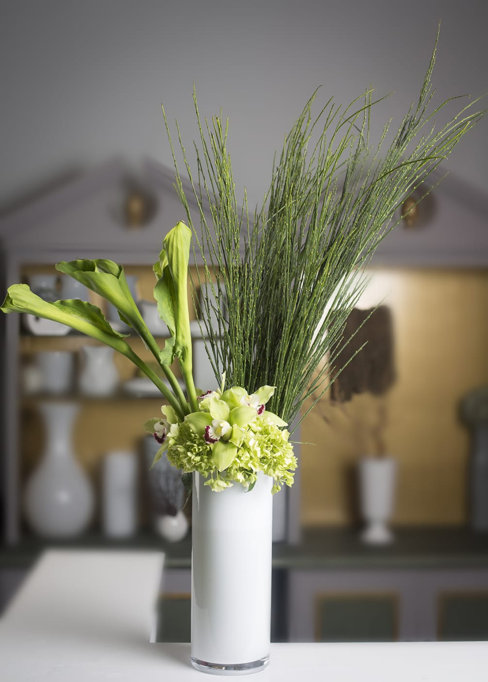 Calla lilies, scotch broom, hydrangea, &amp; cymbidium orchids in a white glass
