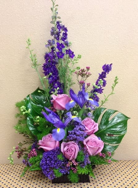Purple roses, iris, larkspur purple and tropical leaves arranged in a black