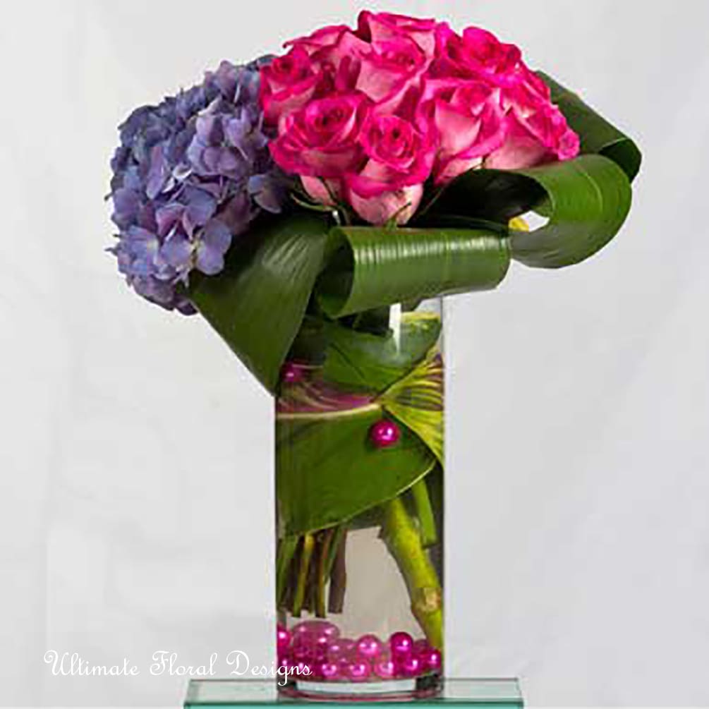Pink roses and purple hydrangeas in a tall glass vase. 