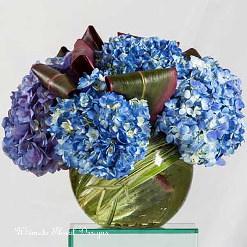 Blue hydrangeas in a round glass vase.