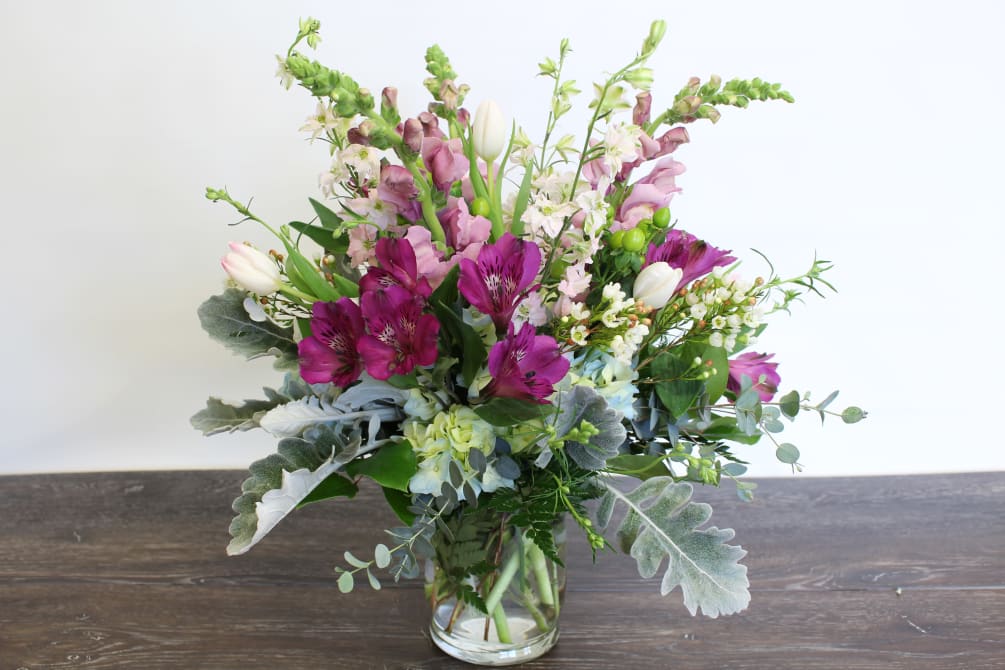 Soft pastel and deep purple flowers fill this hurricane vase to bursting!