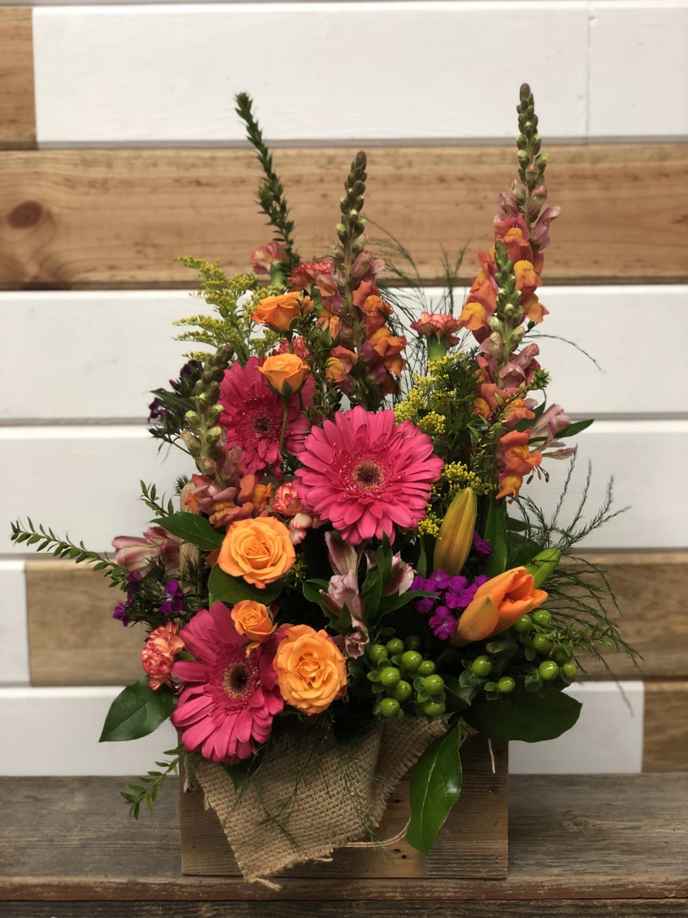 Fresh Gerbera Daisies, hypericum, spray roses and snapdragons fill this low wood
