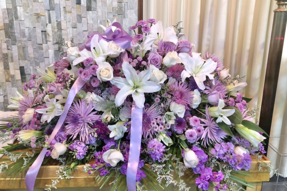 Beautiful lavender and white casket arrangment featuring lillies, dahlias, mums, roses, stock