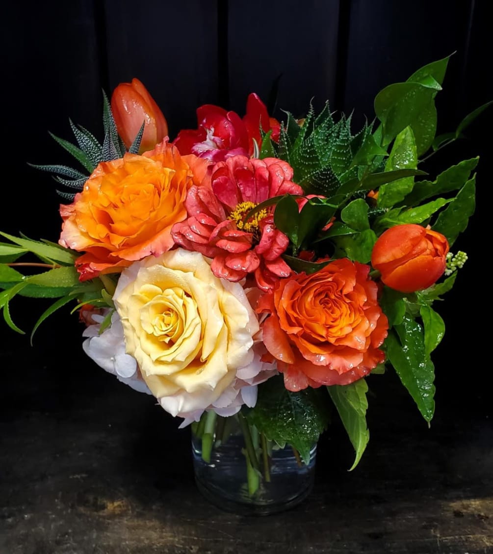 This stunning arrangement features warm colors with a variety of peonies, roses