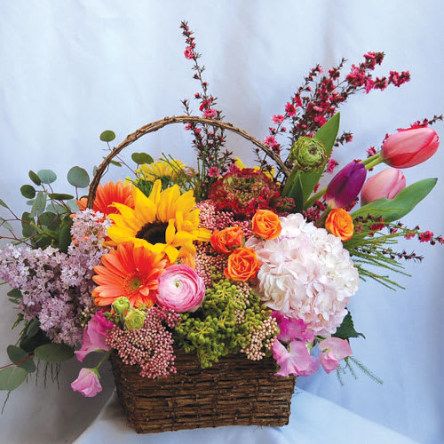 A classic basket filled with seasonal blooms. The arrangement has tulips, sunflowers