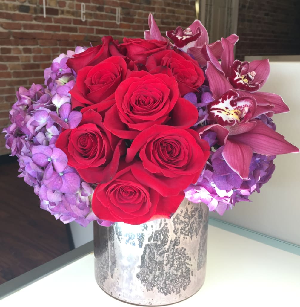 Red roses, purple hydrangea and burgundy cymbidium orchid blooms come together in