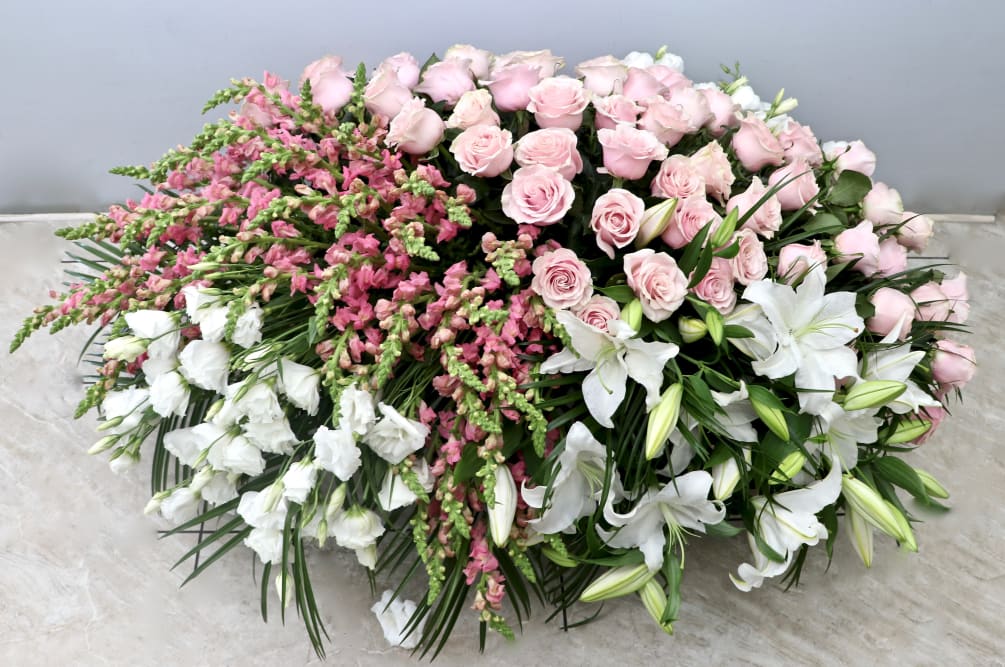 This full casket spray includes pink roses, snap dragons, lisianthus and lilies.