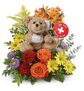 a cute teddy bear nesteled in a bed of flowers