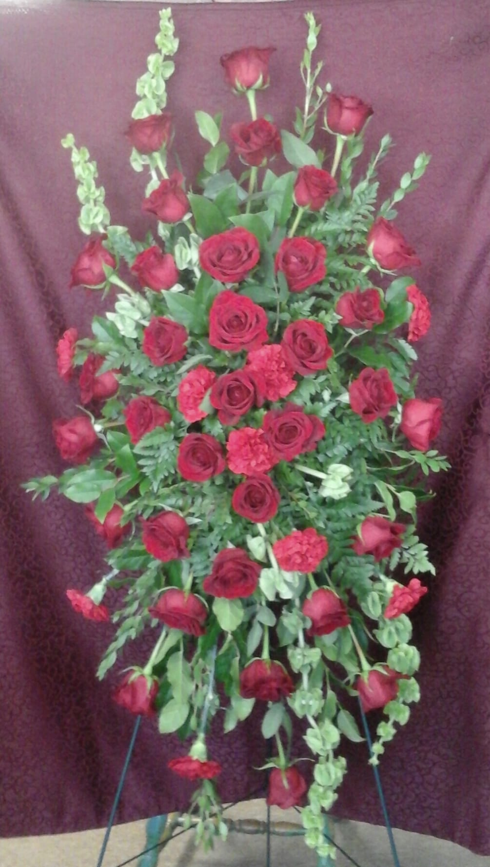 Red roses and carnations spray accented with bells of Ireland 