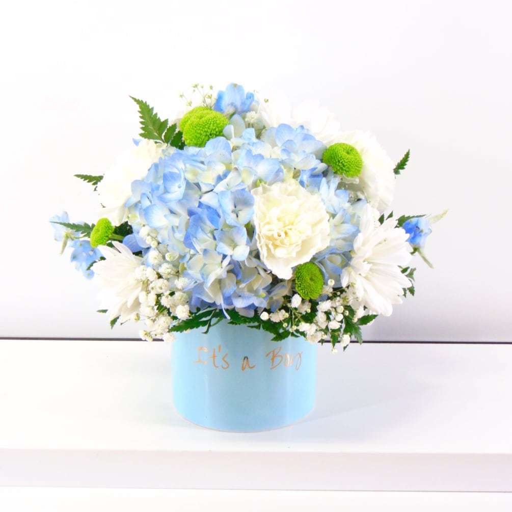 A Keepsake Cylinder Vase filled centerpiece style with blue hydrangea, carnations, daisies