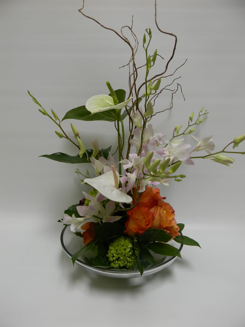 Anthurium, roses and hydrangea designed around curly willow in shallow glass bowl