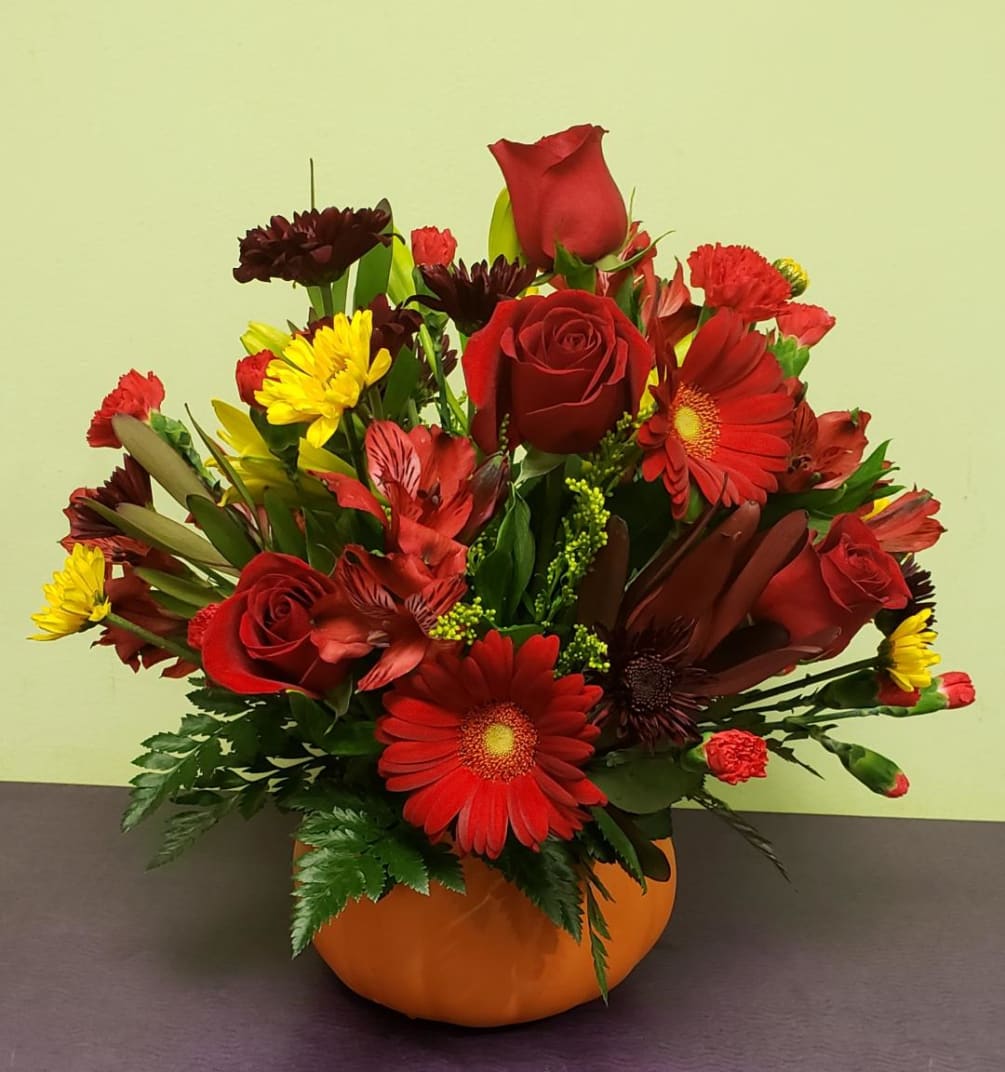 A wonderful ceramic pumpkin container that is filled with fall flowers.